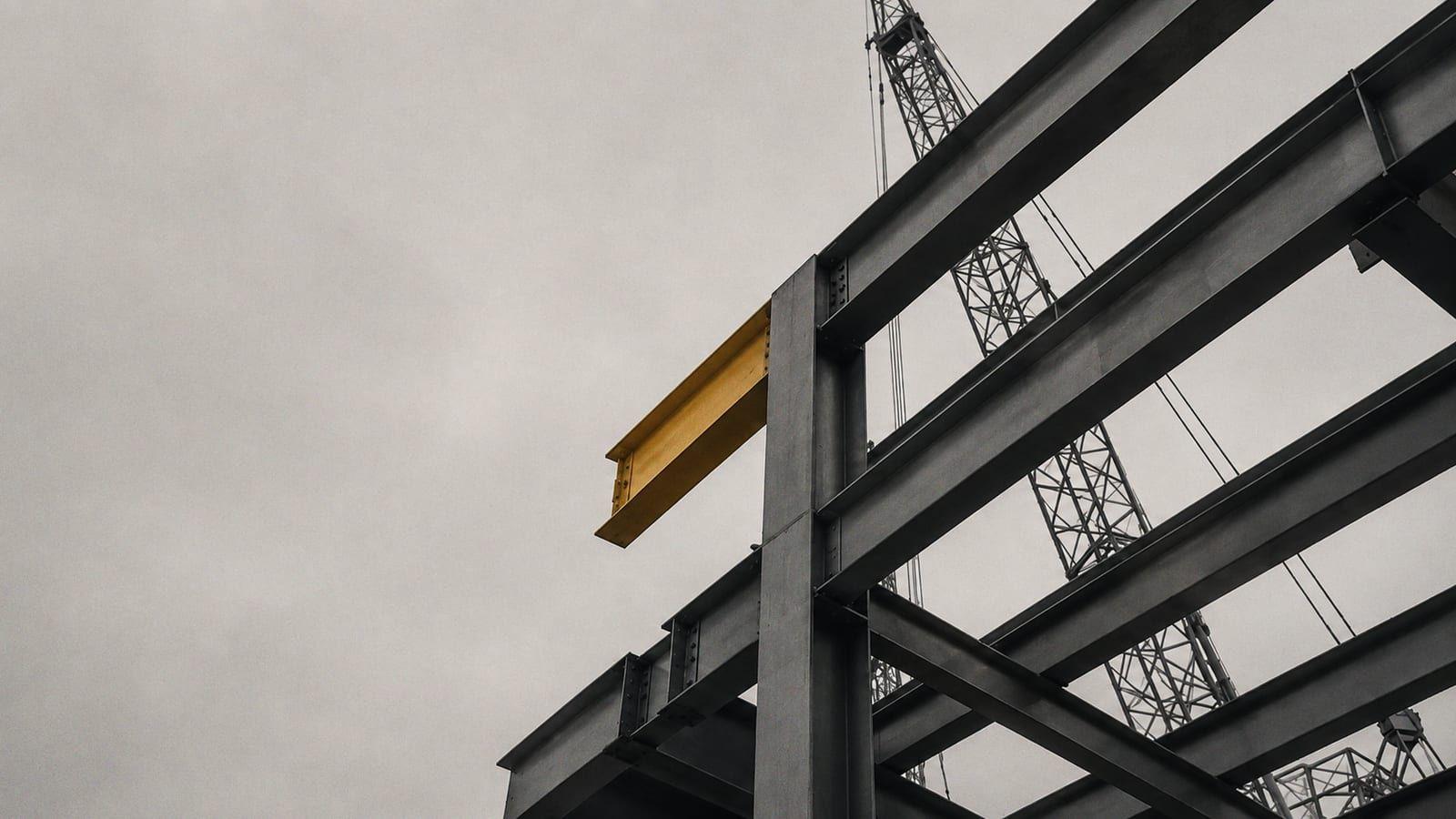 A grey steel frame under a crane, with one beam painted amber