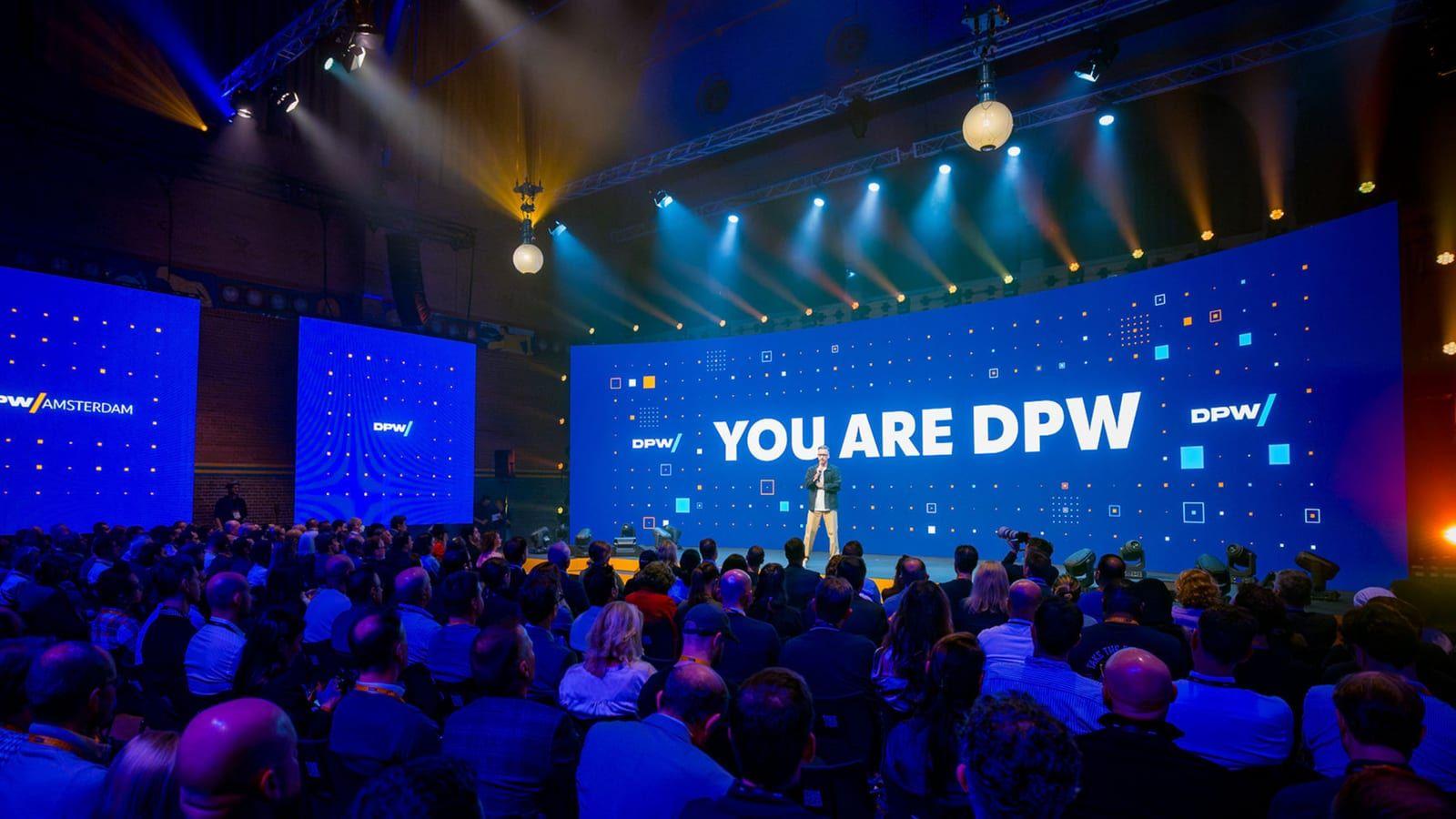 A packed keynote hall at DPW Amsterdam, the main screen reading YOU ARE DPW