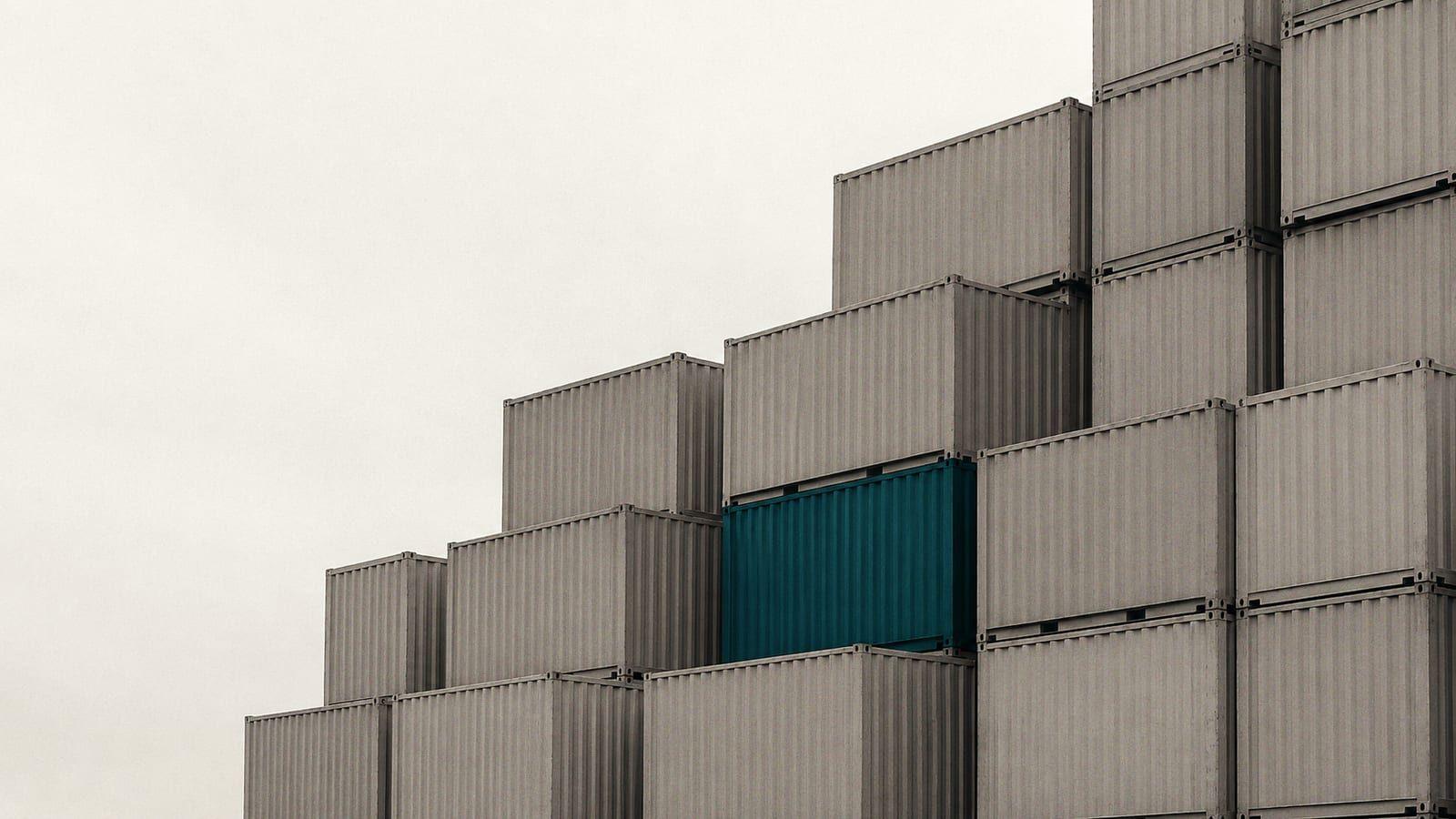Stacked grey shipping containers with a single teal container among them